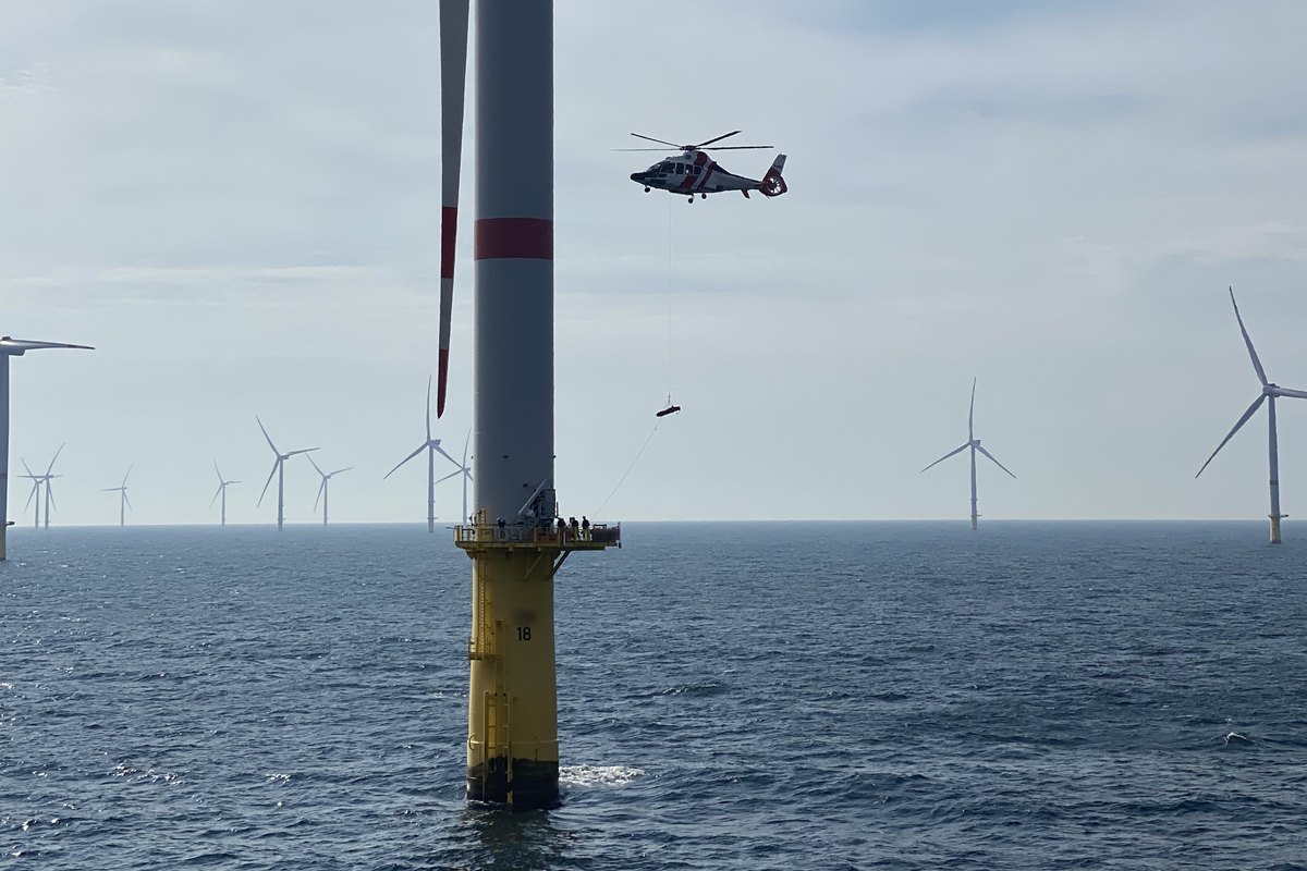 A rescue helicopter winching down to the platform of an offshore wind turbine, with the crew waiting on the deck